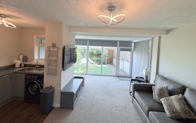 Open-plan living space with kitchen, sofa, storage bench and patio doors to garden