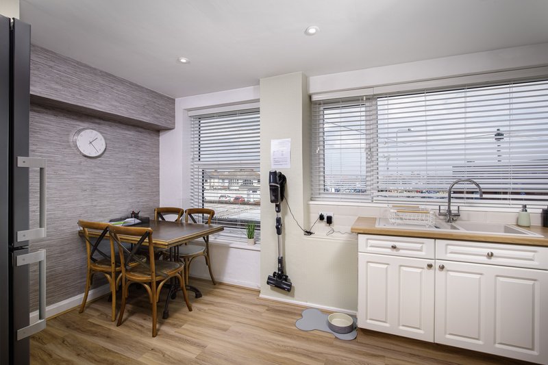 Modern open-plan kitchen and dining area with white cabinetry, wooden dining table, and city views