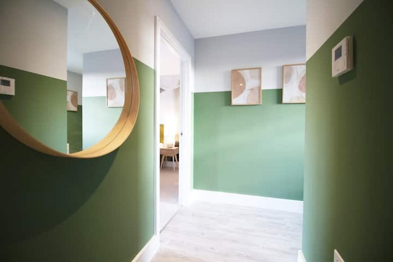Modern hallway with green walls, wooden round mirror, and framed abstract artwork