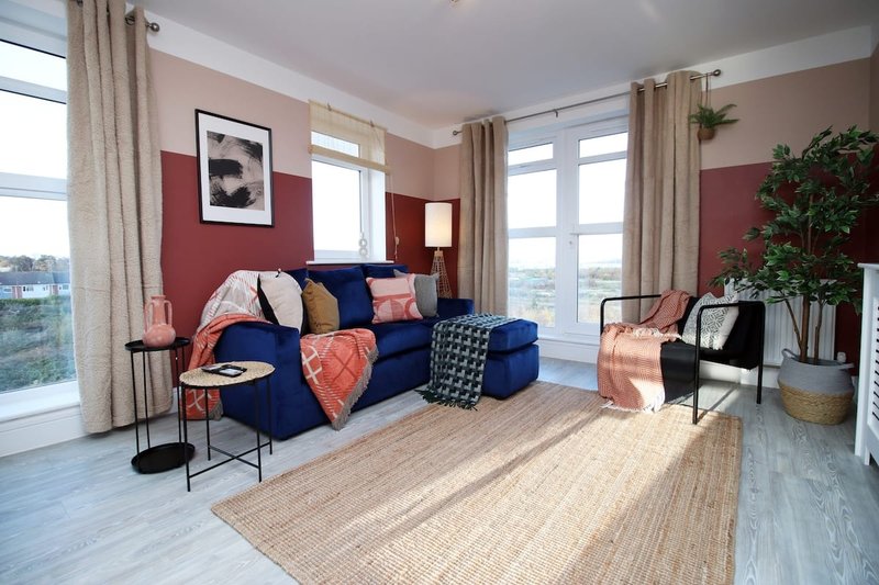Modern living room with blue sofa, red accent wall, large windows and wooden flooring