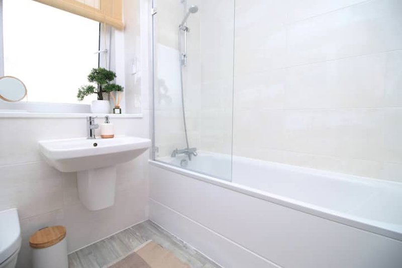 Clean white bathroom with pedestal sink, bathtub, shower enclosure and window