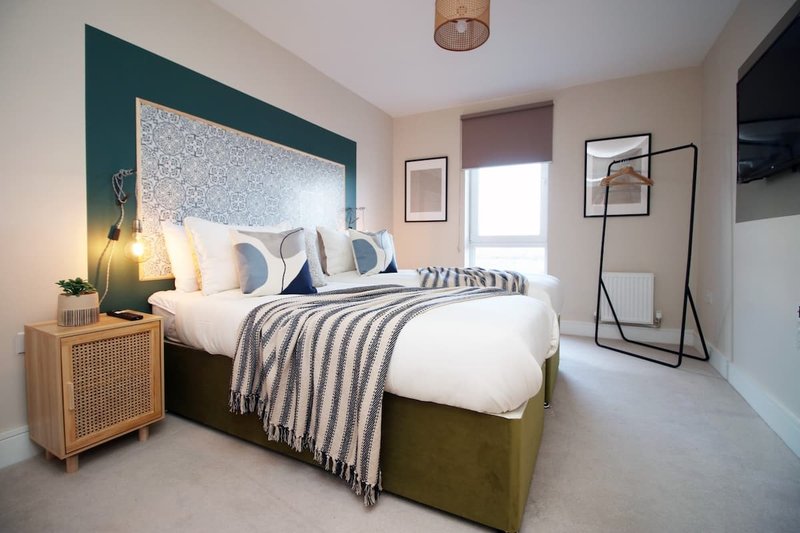 Modern bedroom with olive-green upholstered bed, white bedding, striped throw, and teal accent wall