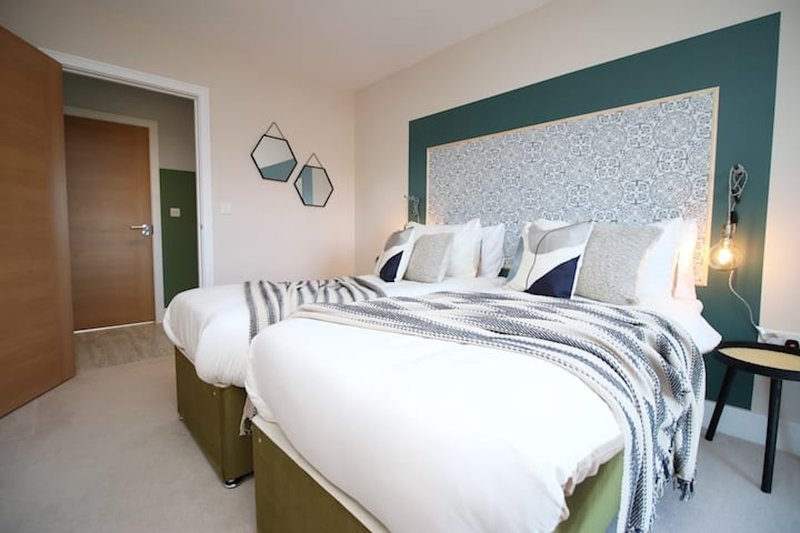 Modern bedroom with double bed, patterned headboard, white bedding, and teal accent wall