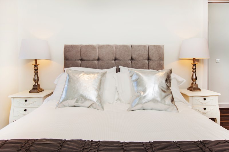 Bedroom with grey upholstered headboard, white bedding, decorative pillows and brass table lamps
