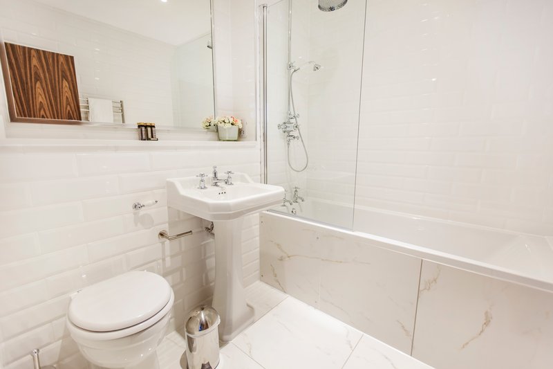 Modern bathroom with white subway tiles, pedestal sink, toilet, bathtub and glass shower enclosure