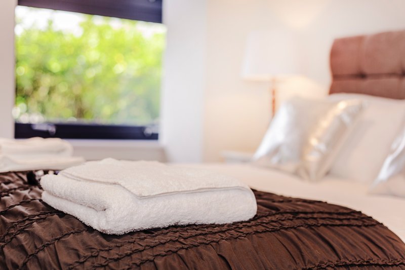 Bedroom with folded white towels on dark bedding, window view, and headboard