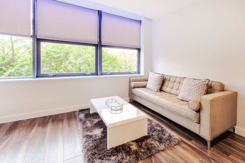 Bright living room with tan sofa, white coffee table, wooden flooring and large windows