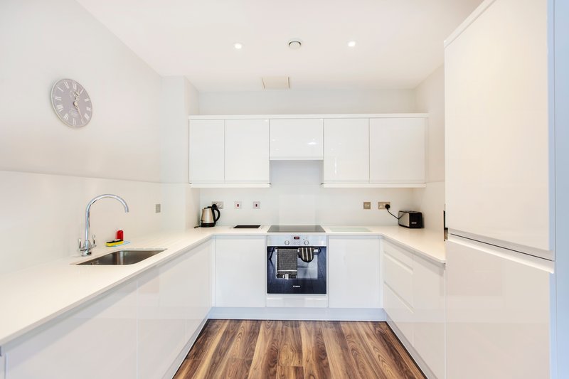 Modern white kitchen with integrated appliances, wooden flooring and wall clock