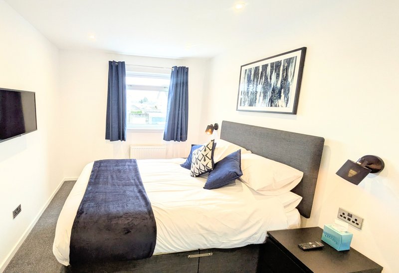 Bright bedroom with double bed, grey headboard, blue curtains and window view