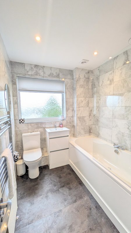 Modern bathroom with bathtub, toilet, sink, tiled walls and window with natural light