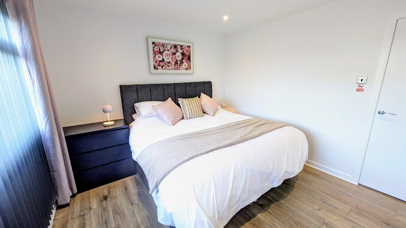 Modern bedroom with double bed, black headboard, cushions, wooden floor and bedside lamp
