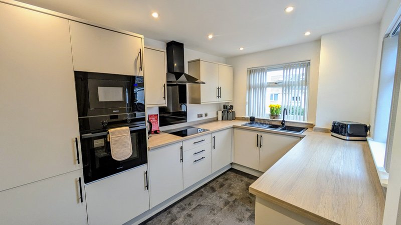 Modern kitchen with white cabinetry, black appliances, wooden countertop and pendant lighting