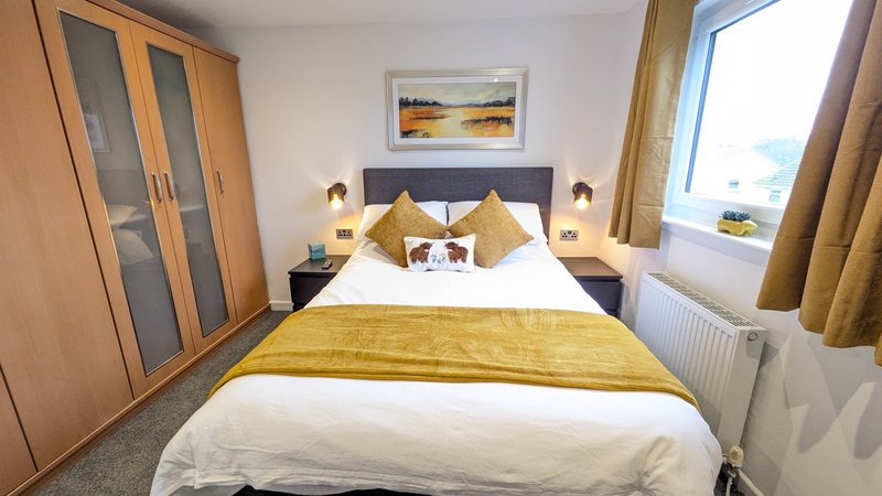 Modern bedroom with double bed, gold cushions, wooden wardrobe and window with curtains
