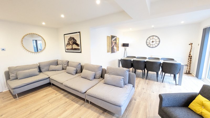 Open-plan living room with large gray sectional sofa, dining table and chairs, wooden flooring and wall art