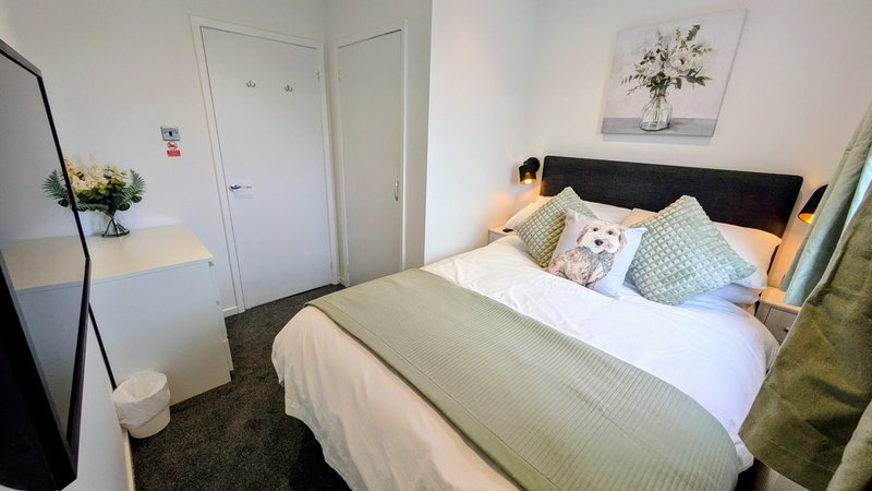 Bedroom with double bed, black headboard, green bedding, wooden nightstands and white doors