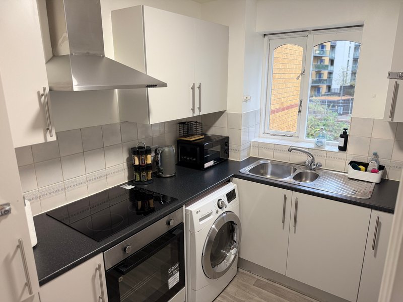 Modern kitchen with white cabinets, black countertop, integrated appliances and window view