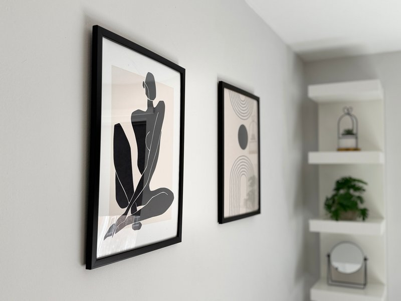 Bright bedroom with framed abstract wall art, white walls, and shelving with decorative items