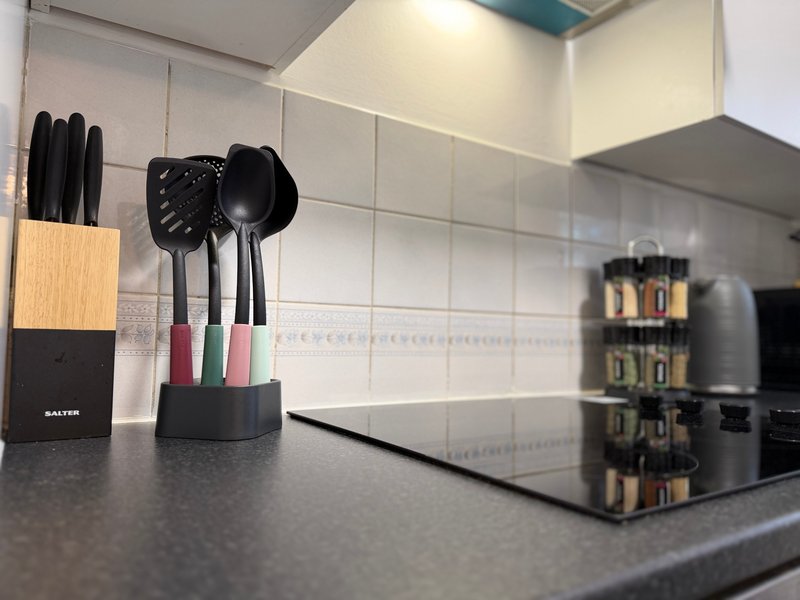 Modern kitchen counter with utensil holder, cooking tools, and spice rack beside stovetop