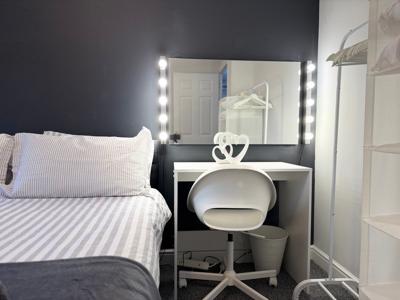 Bedroom with double bed, vanity mirror with LED lights, white desk chair and dressing table