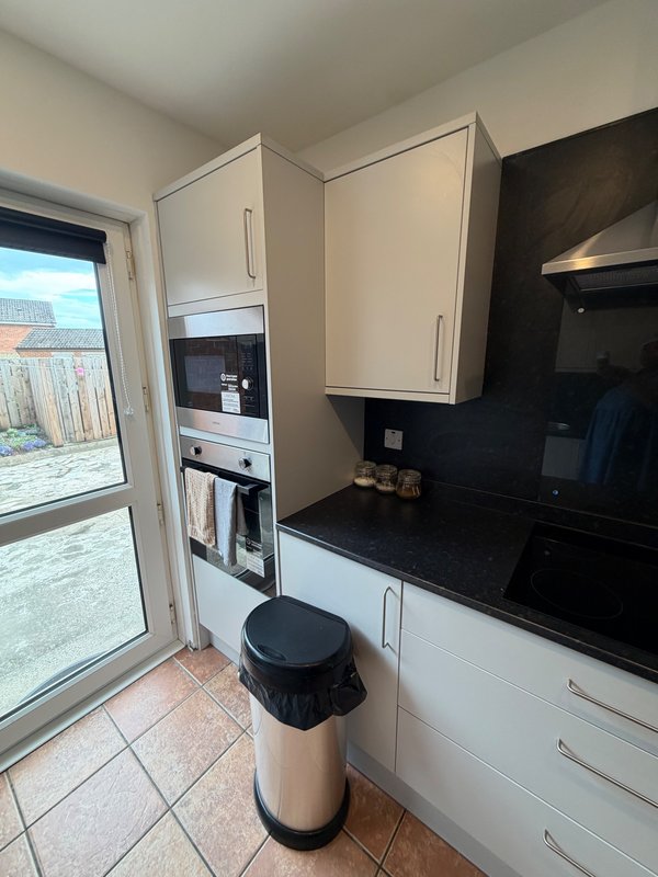 Modern kitchen with cream and black cabinetry, black countertop, built-in appliances and glass door to garden
