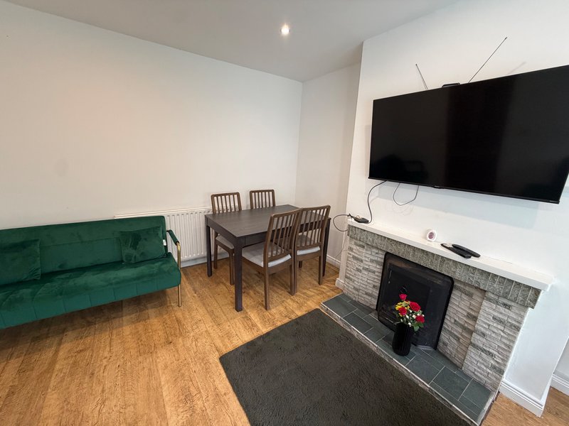 Living room with green sofa, dining table, fireplace, wall-mounted TV and wooden flooring