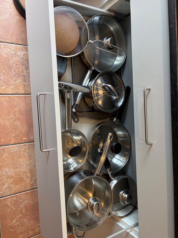 Open kitchen cabinet with stainless steel pots, pans and lids organized inside