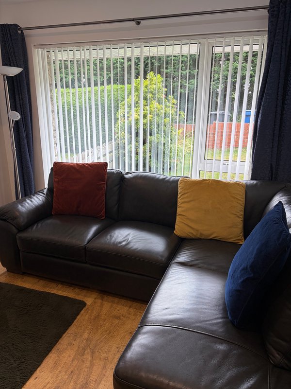 Living room with black leather sectional sofa, colorful cushions, and vertical blinds
