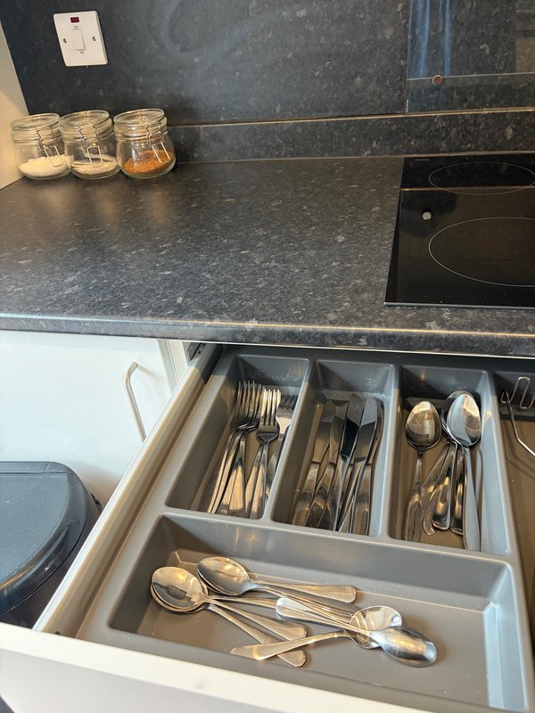 Kitchen counter with dark stone worktop, open cutlery drawer, and glass storage jars