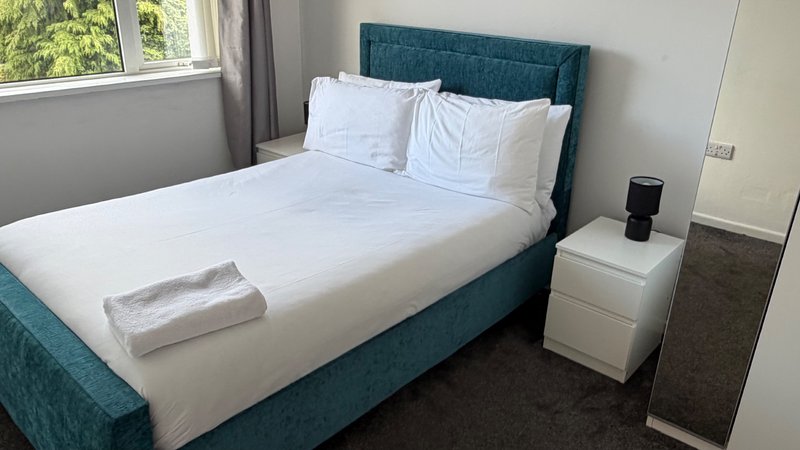 Bright bedroom with teal upholstered bed, white bedding, white nightstand and window with curtains