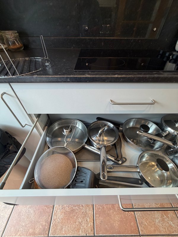 Kitchen drawer open showing stainless steel pots, pans and cooking utensils
