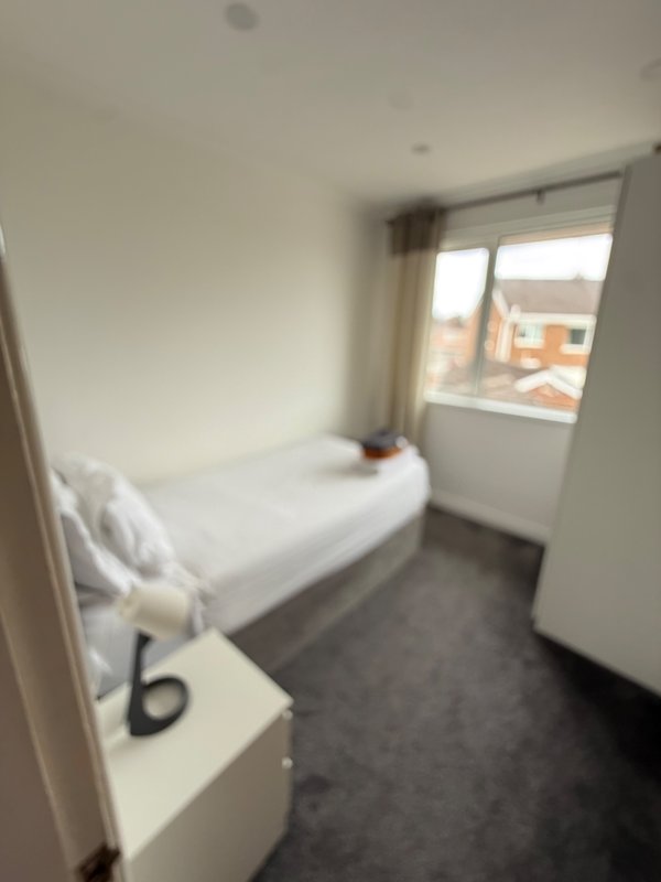 Small bedroom with single bed, white bedding, dark floor and window with curtains