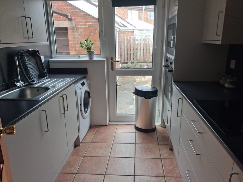 Modern kitchen with washing machine, sink, cabinets and door to garden