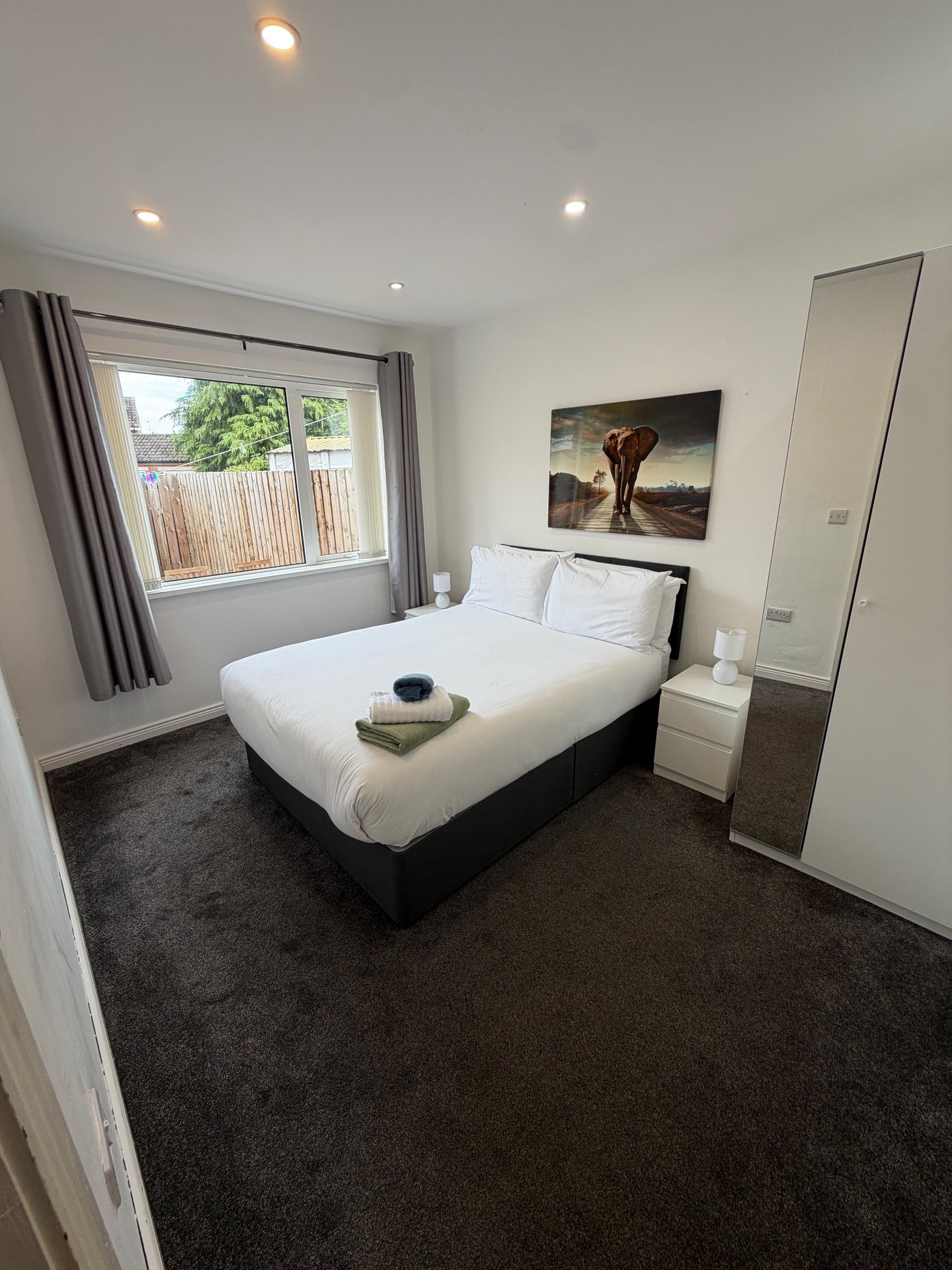 Modern bedroom with double bed, dark carpet, window with garden view, and wall art