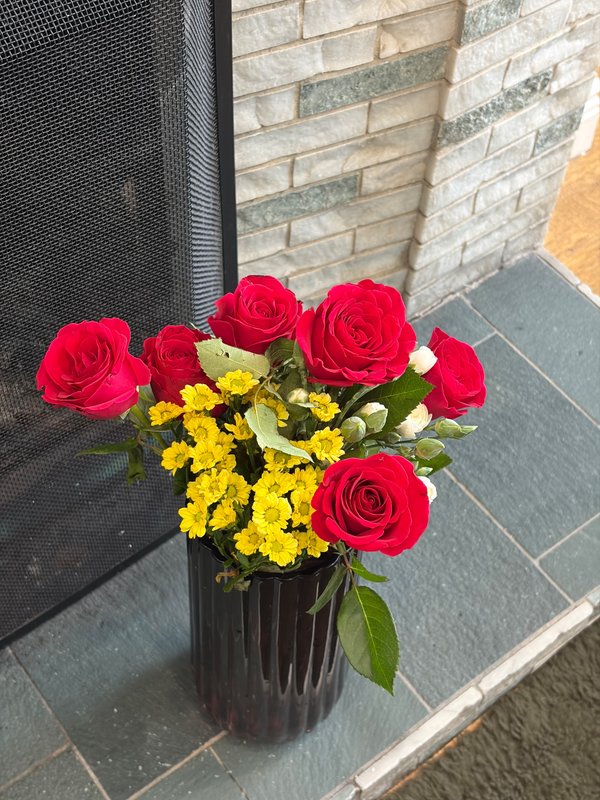 Floral arrangement with red roses and yellow flowers in black vase on patio