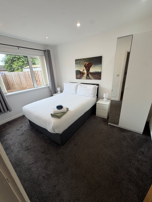 Modern bedroom with double bed, dark carpet, large mirror, and window with garden view