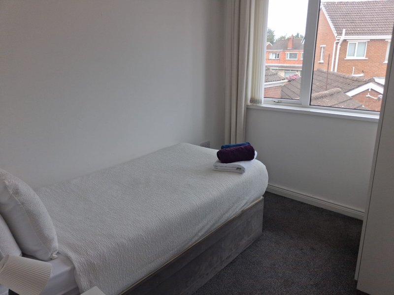 Compact bedroom with single bed, window overlooking residential street, and dark carpet flooring
