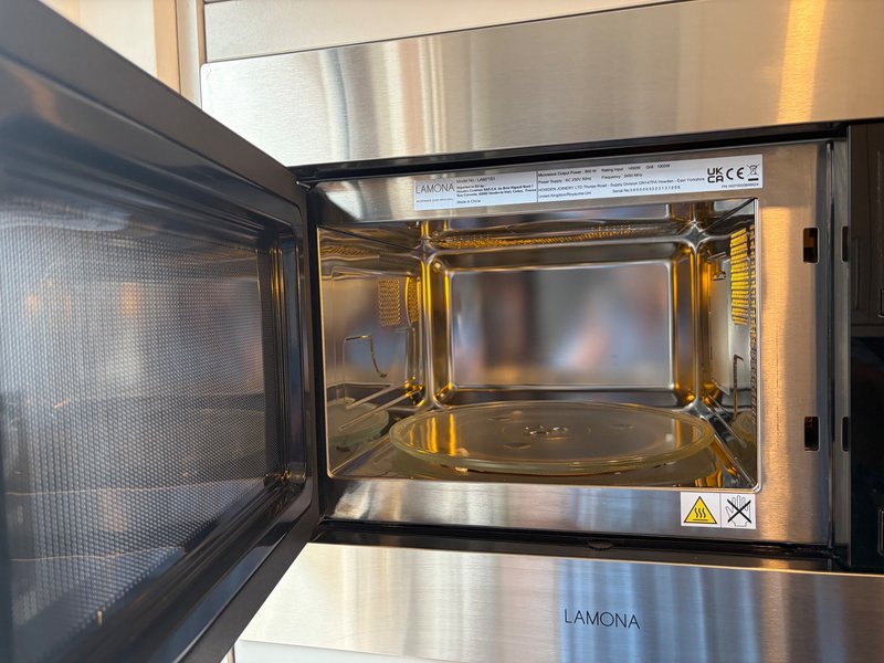 Stainless steel microwave with door open, showing interior cavity and turntable
