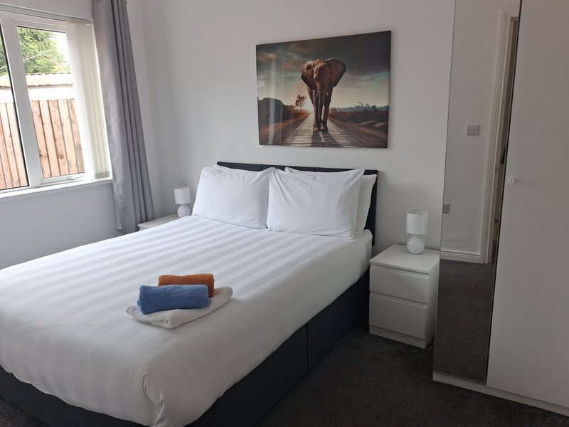 Modern bedroom with double bed, white pillows, folded towels, and elephant artwork above headboard