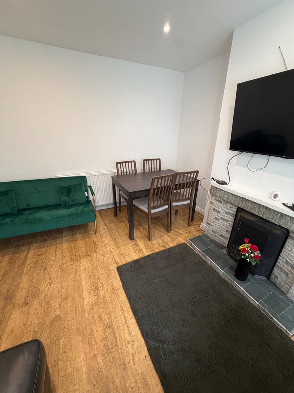 Living room with green velvet sofa, dining table with four chairs, wall-mounted TV and fireplace