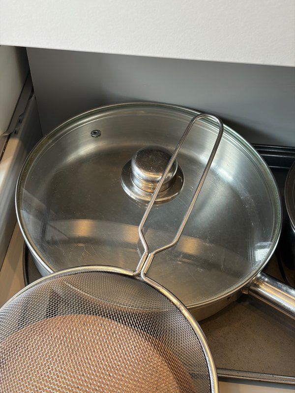 Kitchen cookware including glass lid pot and mesh strainer on stovetop