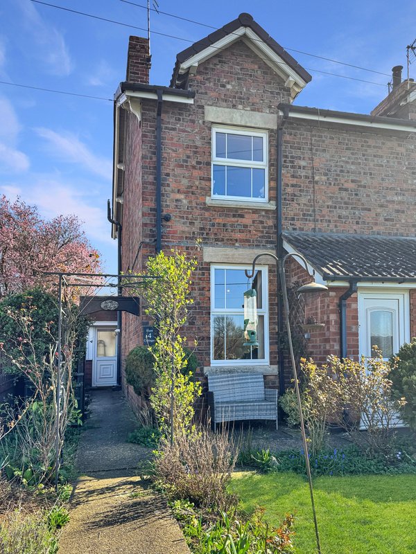 Brick terraced house exterior with front garden, pathway, and ivy-covered walls
