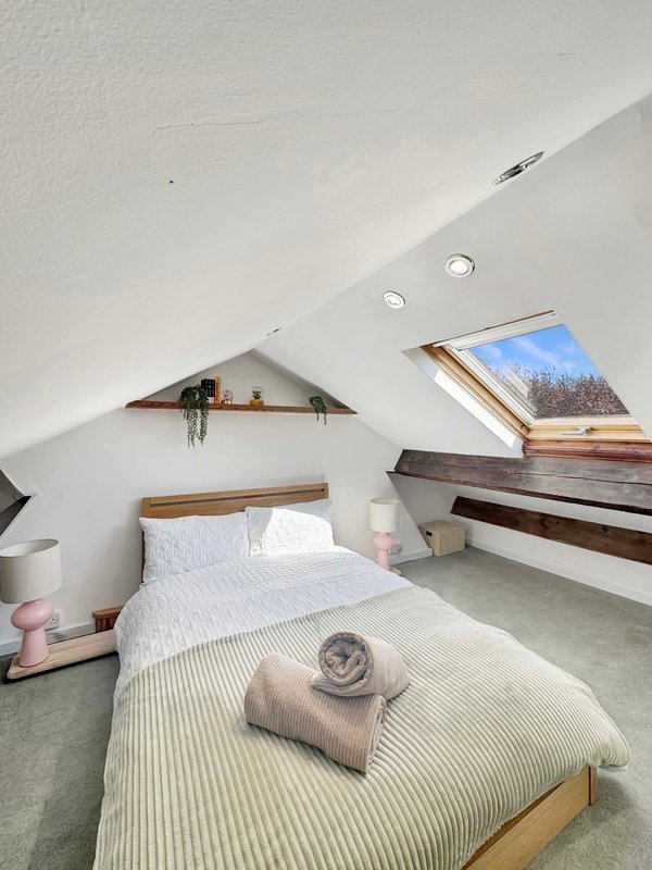 Attic bedroom with single bed, wooden shelving, skylight windows and neutral décor