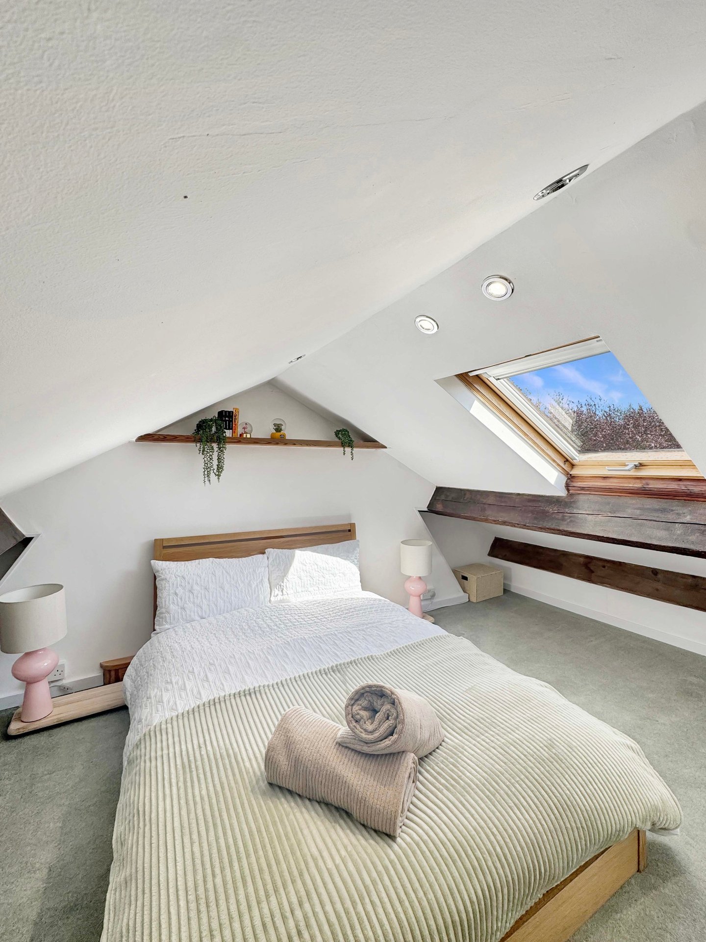 Attic bedroom with single bed, sloped ceiling, wooden shelving and skylight window