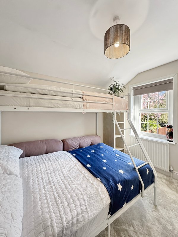 Bright bedroom with loft bed, blue star blanket, cushions, wooden pendant light and window