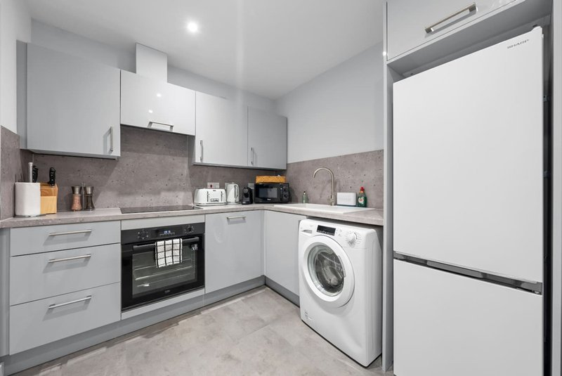 Modern kitchen with white cabinets, gray tile backsplash, built-in appliances and washing machine