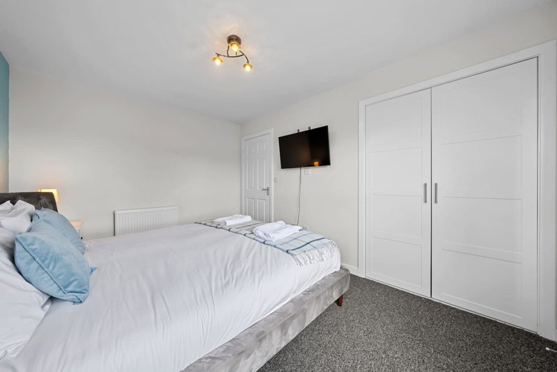 Modern bedroom with double bed, white bedding, wall-mounted TV, and built-in wardrobes