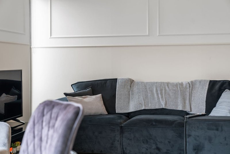 Black upholstered sofa with grey throw blanket, cushions and panelled white wall