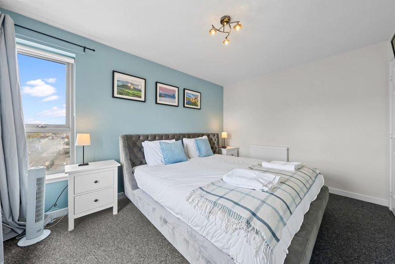 Bright bedroom with double bed, blue accent wall, bedside tables, and large window with countryside view