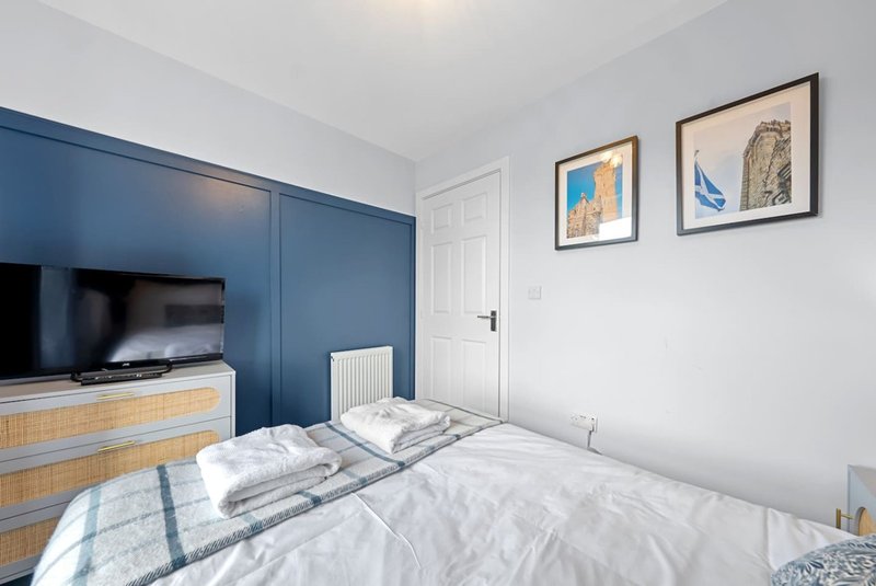 Modern bedroom with double bed, blue wall paneling, wall-mounted TV, and framed artwork