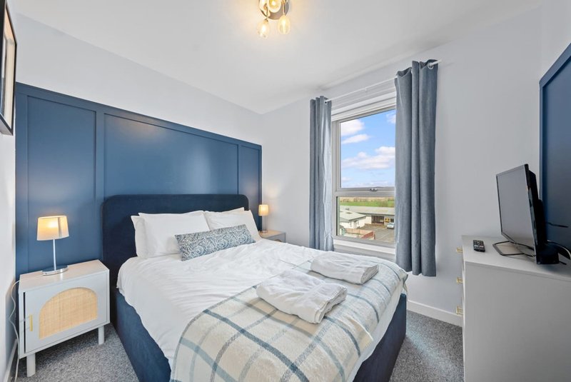 Modern bedroom with double bed, blue headboard, white bedding, and countryside view from window